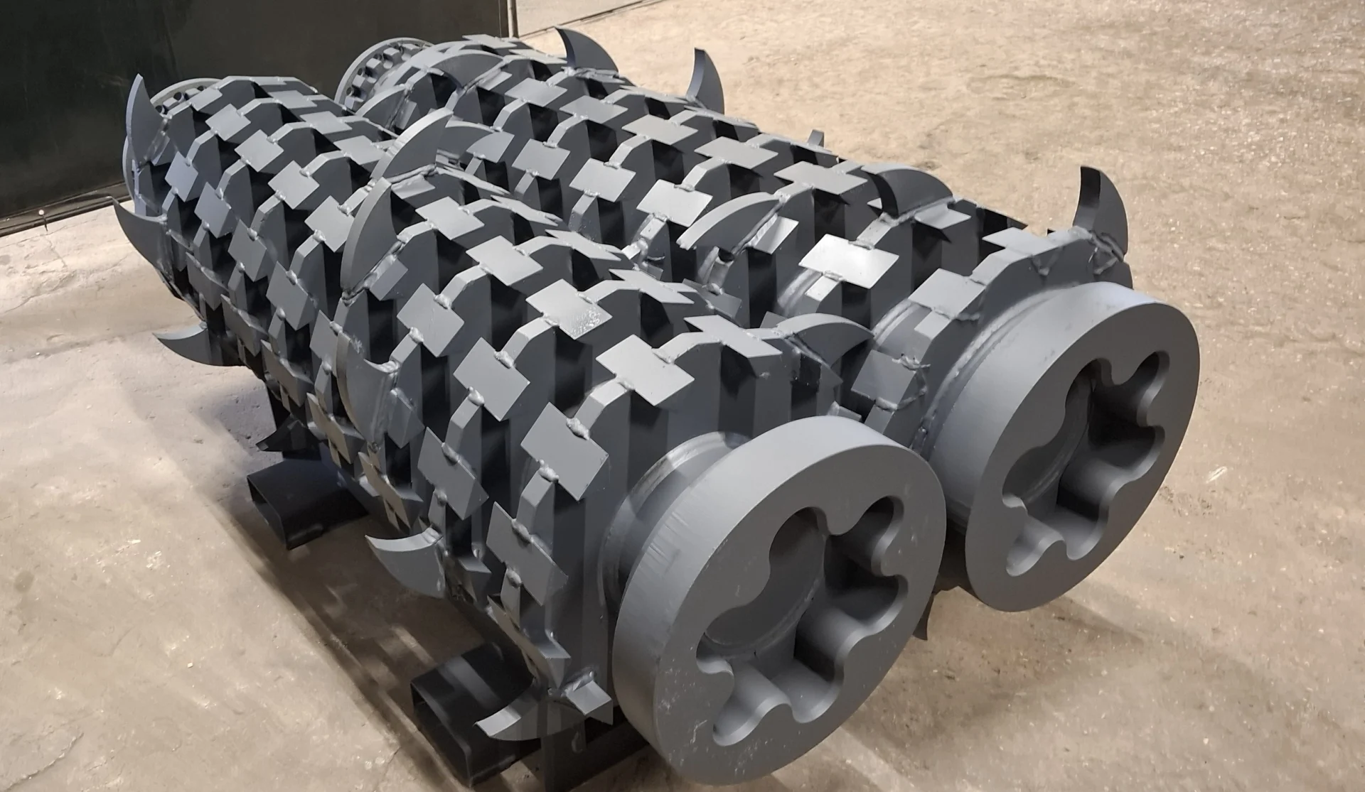 A pair of large, gray industrial shredder T-shafts with distinct cutting teeth and end bearing mounts, ready for heavy-duty shredding applications.