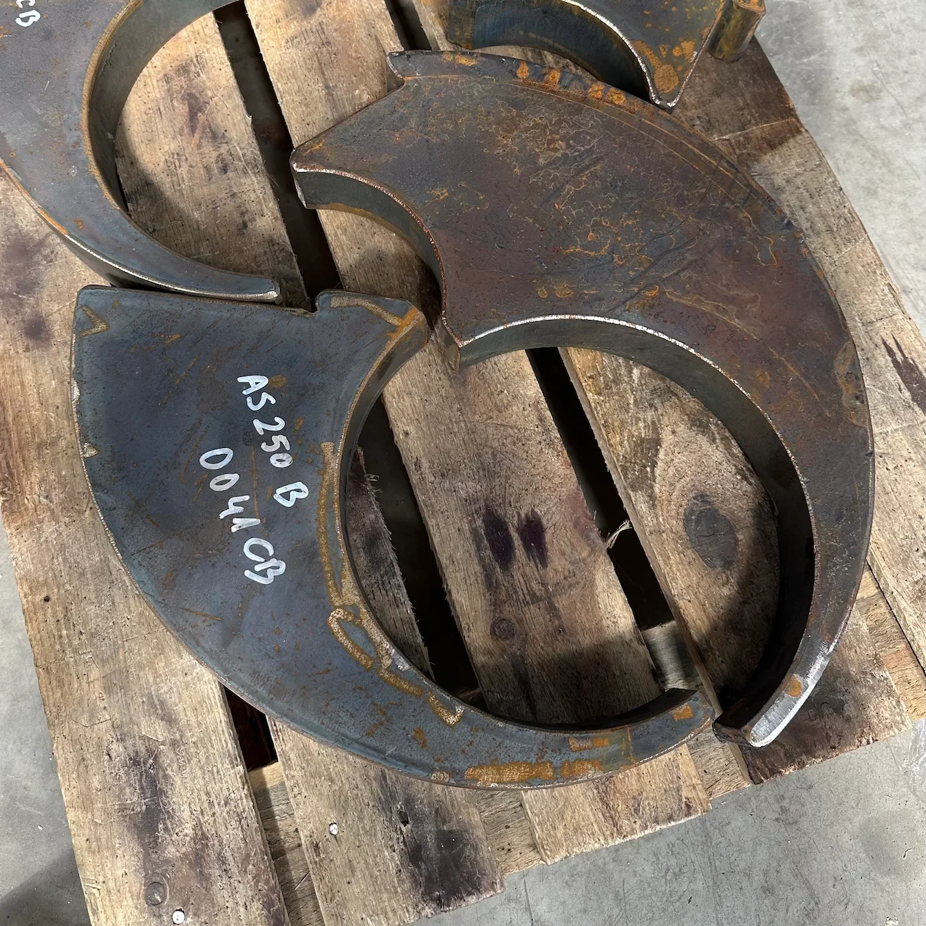 Close-up of a robust, dark grey 403x219x60 CAM V22 concrete shredder shaft made from 400 HB steel, showing its durable construction and precise cut, resting on a wooden pallet.