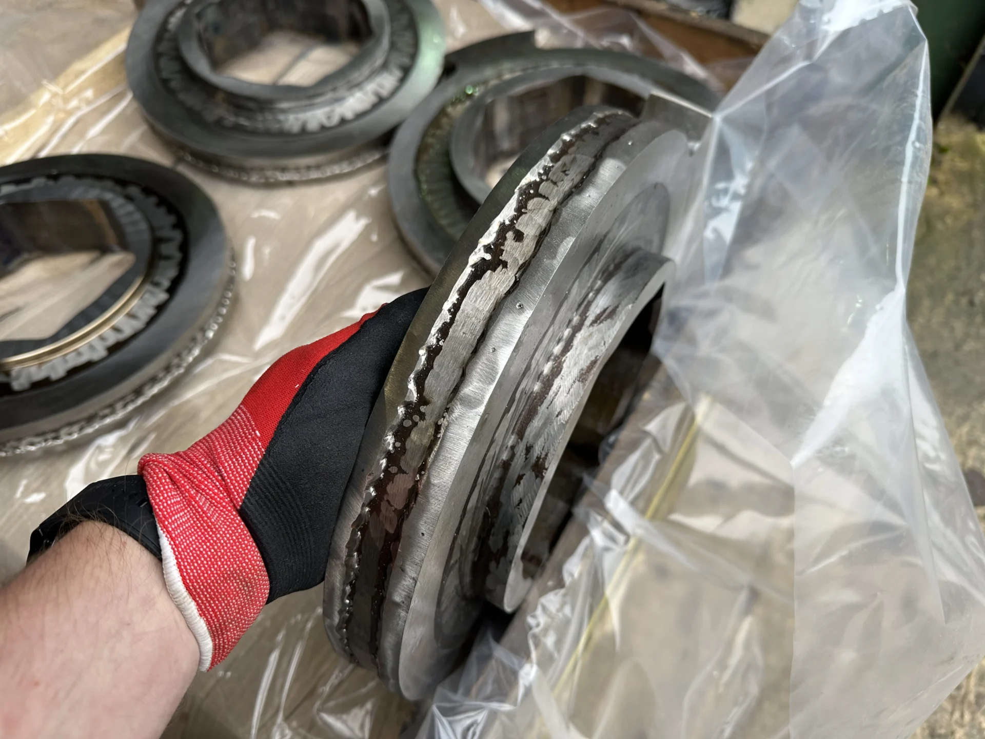 A person wearing a protective glove holding a metal shredder cutter disc showing new wear-resistant weld beads on the outer edge.