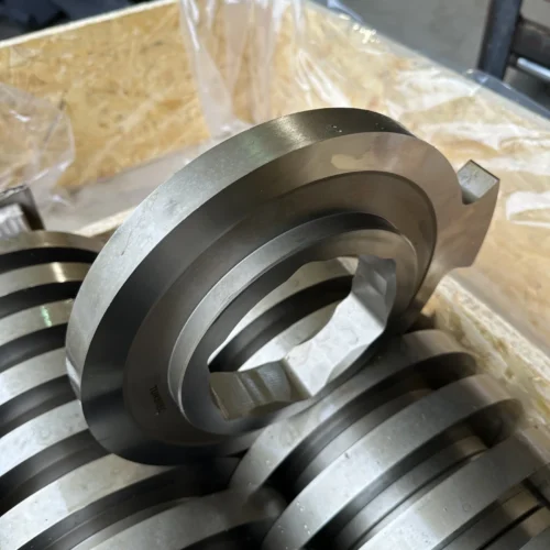 Close-up of a new, metallic TUNSREC cutter unit for UNTHA RS shredders, showing the hexagonal bore and precision finish, stacked in a wooden crate.