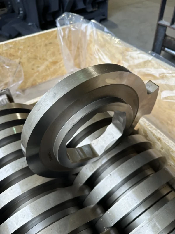 Close-up of a new, metallic TUNSREC cutter unit for UNTHA RS shredders, showing the hexagonal bore and precision finish, stacked in a wooden crate.