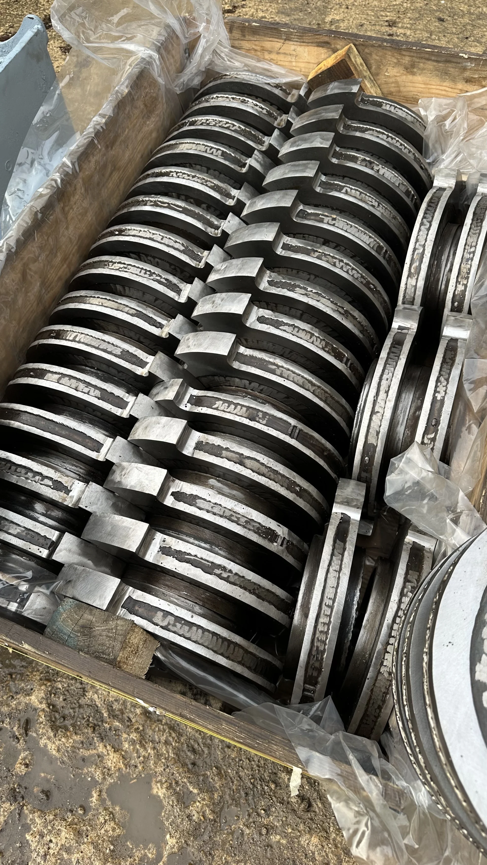 A wooden transport crate containing rows of refurbished and stacked four-shaft shredder cutter discs ready for shipment.