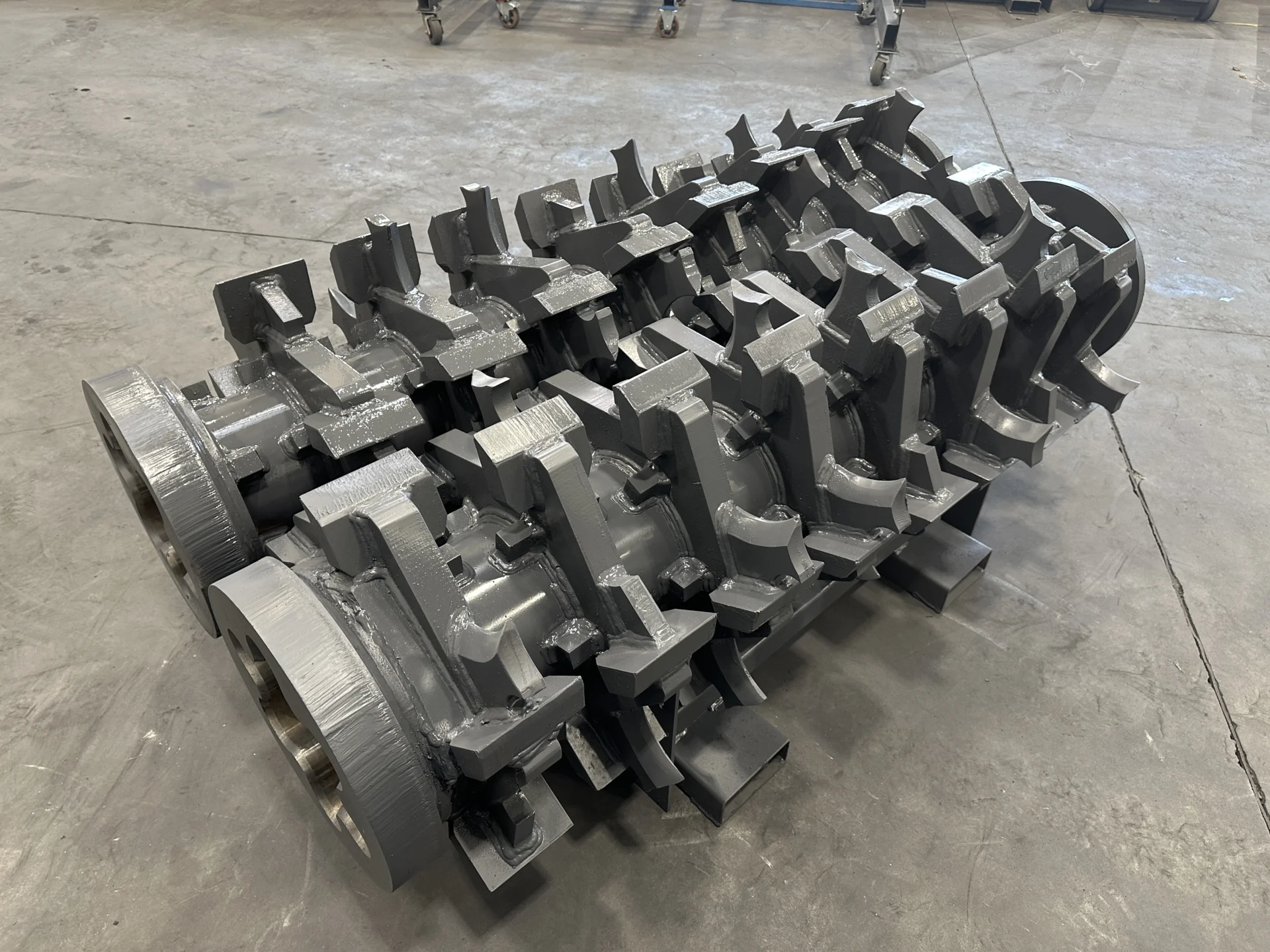 Angled view of two solid shafts equipped with 500 HB knives and 8 discs, designed for Pronar 2.85G biomass shredders, highlighting their robust construction and grey finish.
